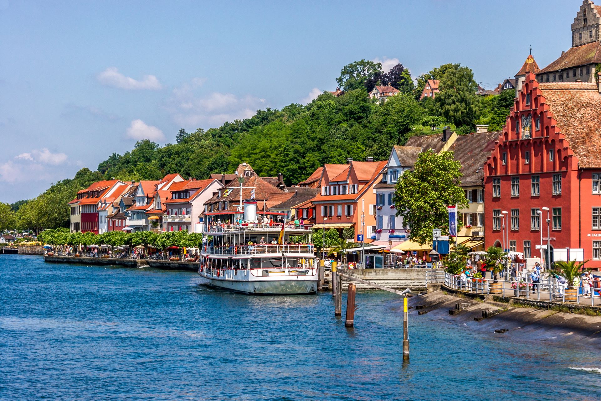 Malerische Uferpromenade in Meersburg am Bodensee mit historischen Fachwerkhäusern, Cafés und einem Ausflugsschiff im Hafen.